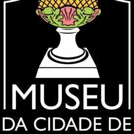Com uma ilustração central de um pedestal branco sustentando uma pinha dourada com detalhes verdes e rosados, simbolizando elemento da arte barroca; abaixo o nome do museu em letras brancas sobre fundo preto, com linhas verticais e horizontais compondo a moldura.