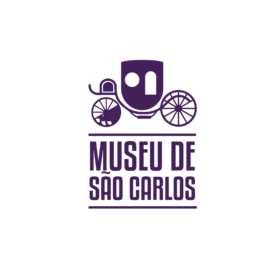 "Logotipo do Museu de São Carlos em roxo. A imagem mostra uma antiga carruagem estilizada com rodas grandes, destacando-se dois círculos representando janelas na parte da cabine. Abaixo da carruagem, está o nome 'Museu de São Carlos' em letras maiúsculas com uma fonte moderna e linhas horizontais acima e abaixo do texto."