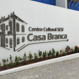 Imagem de uma parede branca com o logotipo do espaço. No logotipo temos o desenho estilizado do casarão seguido do nome "Centro Cultural SESI Casa Branca" na cinza.