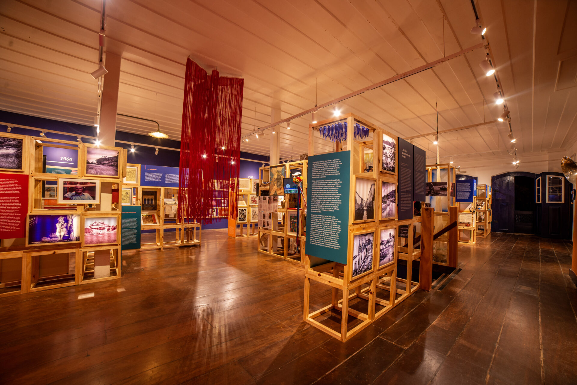 Vista interna da exposição Para uma História Cultural de Paraty: 1945 – 2019, com estruturas de madeira que reúnem fotografias, objetos, documentos e textos.