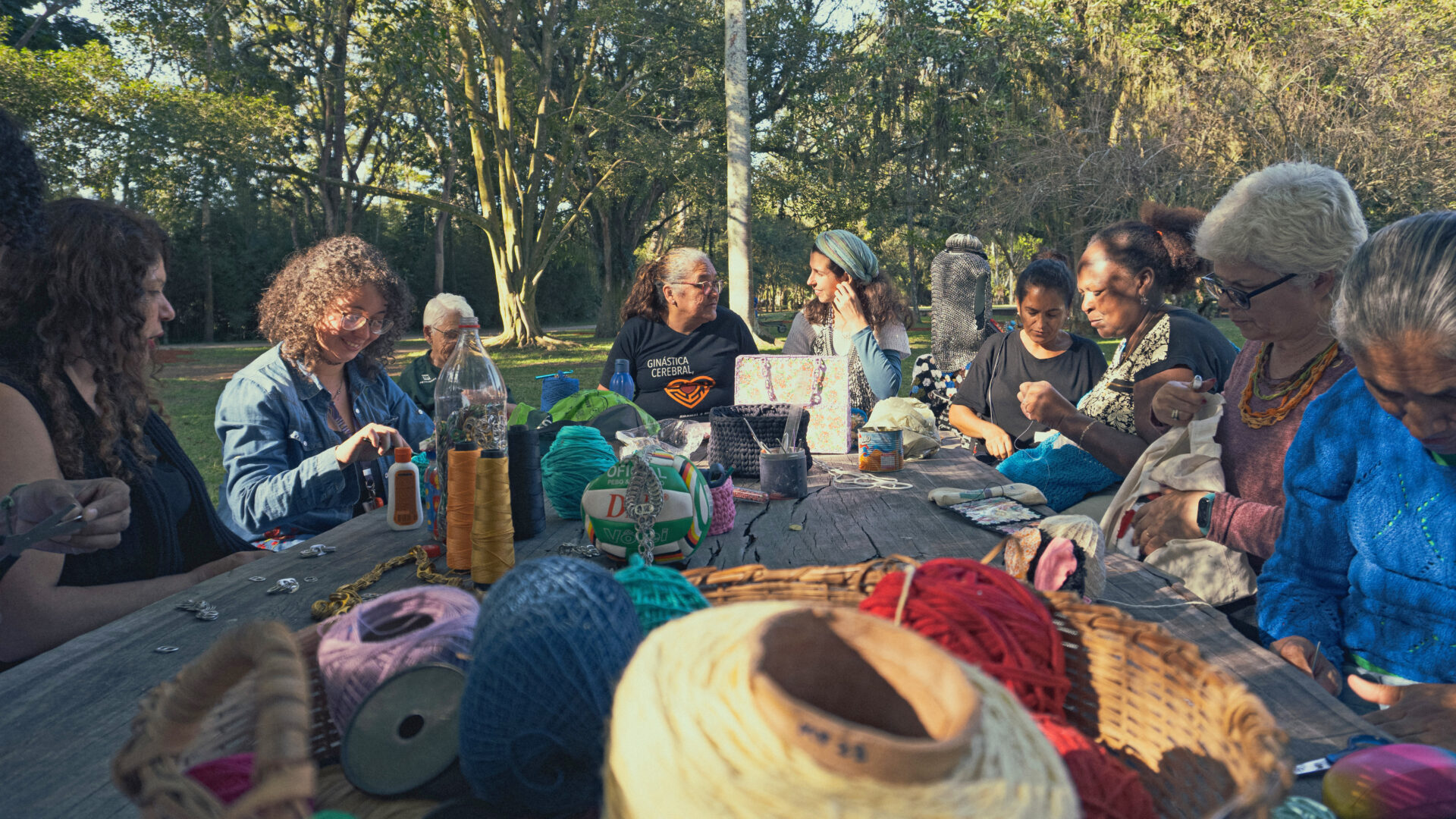 Pessoas de várias idades e etnias, sentadas em volta de uma mesa, fazendo artesanato.